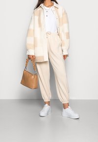 Fleece shirtjack in crèmewit met een beige ruitpatroon, gecombineerd met beige joggingbroeken en witte platform sneakers, en een tan handtas.