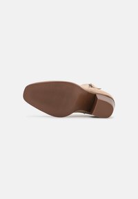 Beige suede shoe sole with a textured brown rubber outsole. Upper features a low heel and side zipper detail. Smooth finish overall.