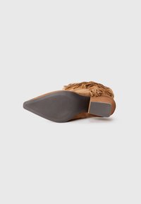 Brown suede ankle boot with fringed detailing, pointed toe, and a textured rubber outsole. Light brown heel accent at the rear.