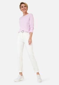 Pull léger rose à manches longues, jeans blancs et baskets blanches. Les jeans sont ajustés avec un revers, et la ceinture est en métal argenté.