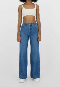 Kevyt rajattu valkoinen toppi leveillä olkaimilla yhdistettynä korkeahintaiseen, leveälahkeiseen keskisiniseen farkkukenkäpariin. Valkoiset lenkkarit viimeistelevät ilmeen.