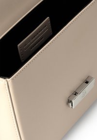 Sac à main en cuir beige avec une texture lisse, doté d'une fermeture en métal argenté et d'une étiquette intérieure indiquant "Limited Colors of Benetton."