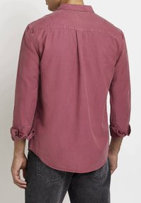 Camicia a maniche lunghe di colore rosa polveroso, realizzata in tessuto morbido. Presenta un colletto a bande, polsini arrotolati e una leggera piega sul retro.