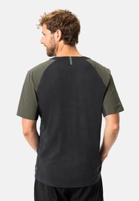 Camisa negra de manga corta con detalles en verde oliva y perforaciones en las mangas, que presenta un diseño minimalista y un corte recto.