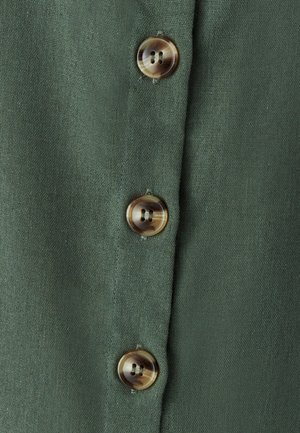 Tela de color verde oliva con un acabado texturizado, que presenta tres botones redondos de dos agujeros en un color claro y contrastante. Tapeta de botones vertical.