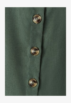 Olivově zelená látka se třemi hnědými knoflíky, každý s dvěma otvory, na texturovaném pozadí připomínajícím len.