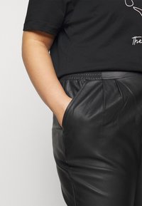 Czarne skórzane spodnie z elastycznym paskiem w talii i bocznymi kieszeniami, w połączeniu z czarną koszulką z minimalistycznym wzorem linii.