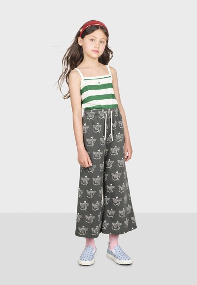 Stribet grøn og hvid tanktop parret med brede grå bukser med et mønsterdesign. Blå slip-on sko og lyserøde sokker fuldender outfittet.