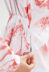 Main tirant la fermeture éclair d'une veste rose et blanche à motifs avec poignets et taille élastiques, montrant un gros plan de la texture du tissu.