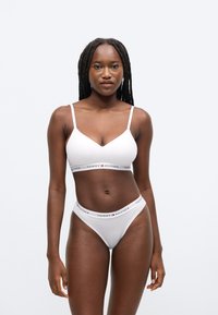 Biely bralette a zodpovedajúce tangá s logom Tommy Hilfiger na páse. Bralette má nastaviteľné ramienka a trojuholníkový dizajn.