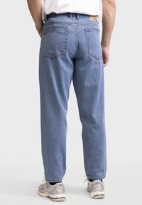 Vaqueros de denim azul claro con corte recto, costuras visibles, dos bolsillos traseros y una etiqueta de cuero en la cintura. Combinados con zapatillas grises.