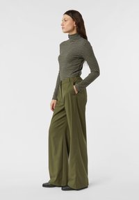 Zielony prążkowany golf o dopasowanym kroju, zestawiony z oliwkowymi, szerokimi spodniami z wysokim stanem. Gładka faktura i widoczne boczne kieszenie.