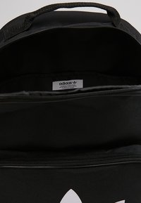 Black backpack with a zip closure, interior lining, and an Adidas logo tag visible. Features a textured exterior and sturdy carrying handle.