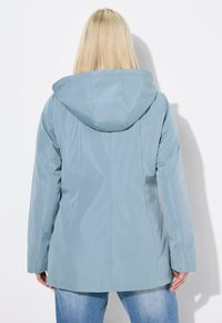 Ljusblå vattentät jacka med huva, med långa ärmar, en åtsittande silhuett och en slät, matt yta. Enkel design utan synlig hårdvara.