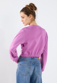 Lilla, kort sweatshirt med lange ermer, ribbestrikket midje og rund hals, kombinert med høyt midje blå denim jeans.