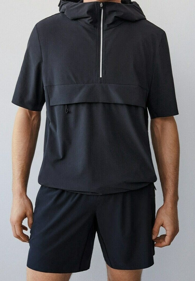 Conjunto atlético negro que incluye una camiseta de manga corta con cuello con cremallera, un bolsillo frontal y pantalones cortos a juego, todo en una tela ligera y suave.