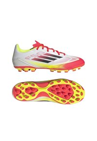 Valkoiset ja punaiset jalkapallokengät mustilla yksityiskohdilla. Teksturoitu synteettinen päällinen, limevihreä kaulus ja monivartiset keltaiset pohjat.