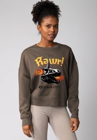 Sweat-shirt marron avec une impression graphique représentant un crâne de dinosaure et du texte. Poignets et ourlet côtelés. Assorti à un legging côtelé clair.