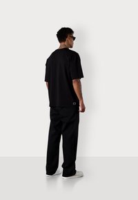 T-shirt noir à manches courtes avec une coupe décontractée, associé à un pantalon noir ample et des baskets blanches, présentant un design minimaliste et sans logos visibles.