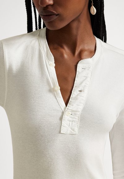 Λευκό μακρυμάνικο τοπ από υφή υφάσματος, με κουμπωτή λωρίδα και τρία κουμπιά, καθώς και V-σχήματος λαιμόκοψη.