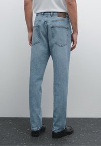 Light blue denim jeans with a relaxed fit, featuring two back pockets and a brown leather patch on the waistband. Smooth texture and simple design.