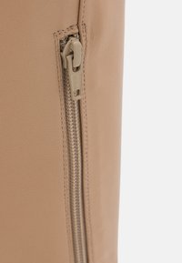 Gros plan sur un matériau en cuir beige avec une fermeture éclair YKK beige assortie partiellement ouverte verticalement.