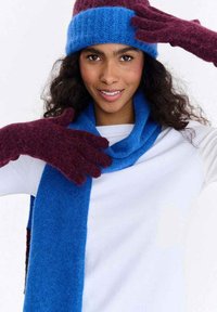 Zestaw zimowy z wełnianą czapką, szalikiem i rękawiczkami. Czapka w kolorze niebieskim i bordowym, szalik niebieski, rękawiczki bordowe, wszystkie o miękkiej fakturze i dzianym wzorze.