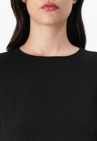 Top negro de manga corta con cuello redondo, hecho de tela texturizada; presenta una superficie lisa y uniforme sin patrones visibles.