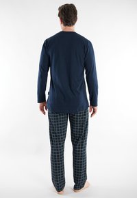 Navy long-sleeve shirt with a smooth texture paired with plaid pajama pants in dark blue and yellow grid pattern. Casual loungewear set.