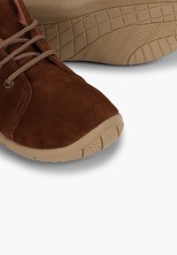 Scarpe in suede marrone con una texture morbida, punta rotonda e suola in gomma beige con un motivo a onda per la trazione. I lacci sono di un colore beige abbinato.