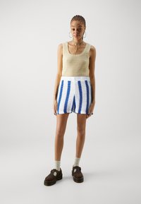 Top de ganchillo en color beige con bordes en pico, combinado con pantalones cortos de punto a rayas en azul y blanco. Zapatos de plataforma marrones y calcetines claros.