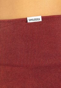 Cintura elastica bordeaux con texture a coste, etichettata "SMILODOX." Tessuto liscio, design aderente, adatto per abbigliamento sportivo.