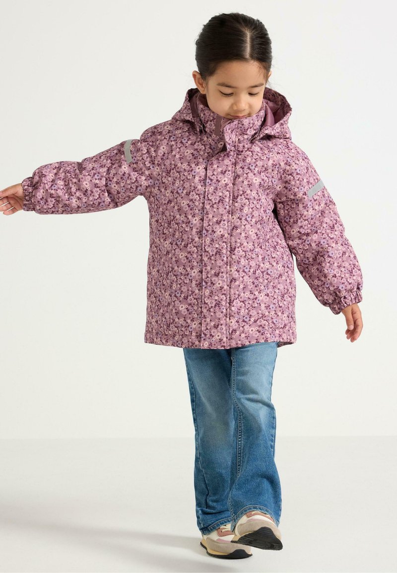 Paarse winterjas met bloemenpatroon, hoge kraag, elastische manchetten en capuchon; gecombineerd met lichtblauwe jeans en sneakers.