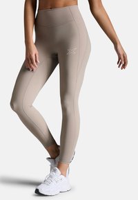 Beige hochgeschnittene Leggings aus dehnbarem Stoff, mit gerippten Details am Bund und einem kleinen Logo-Highlight am Oberschenkel.