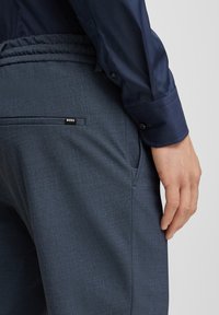 Navyblå byxor med texturerat tyg, med en rynkad midja och en liten svart "BOSS"-logotyp på bakfickan.