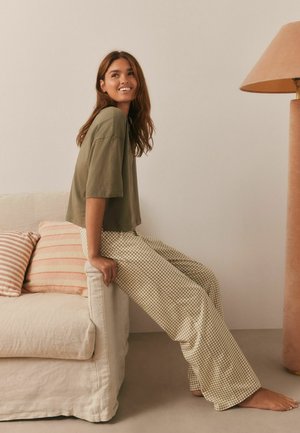 Casual outfit featuring an olive green cropped shirt and beige checkered wide-leg pants, seated on a cream-colored sofa with striped pillows.