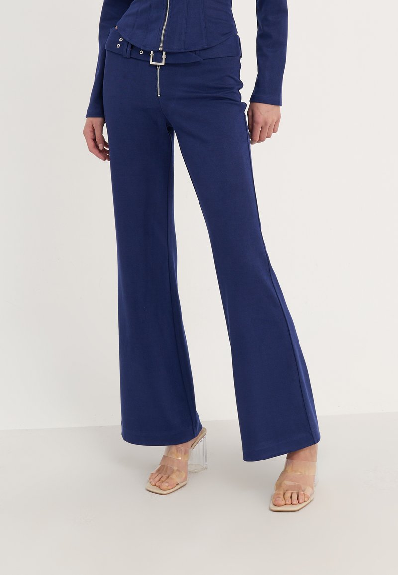 Navyblauwe fitted top met een rits, gecombineerd met wijde navybroek. Gestructureerde stof en detail van een zilveren riemgesp. Transparante sandalen.