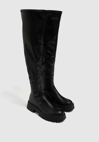 Bottes noires cuissardes avec une tige synthétique lisse et brillante, une semelle en caoutchouc épaisse et une fermeture éclair latérale contrastant avec le matériau texturé.
