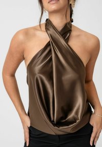 Brązowa satynowa bluzka z skręconym dekoltem na halter, w fałdowanym kroju i gładkiej fakturze. Połączona z czarnymi spodniami o prostym fasonie.