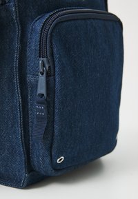 Traper torba s teksturiranim tamnoplavim materijalom, s džepom na zatvarač, ojačanim dnom i metalnom okomicom za dodatnu izdržljivost.