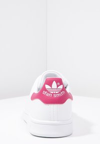 Vit lädersneaker med en rosa läderheel-tab. Har präglad "stan smith" och tre-strekslogotyp. Slät textur, låg design.