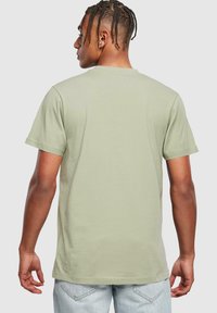 Lys grøn kortærmet bomulds t-shirt set fra ryggen. Har en klassisk rund halsudskæring og en afslappet pasform, parret med lyseblå jeans.