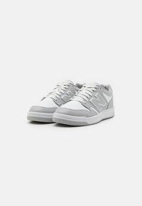 Hvide og lysegrå sneakers med et perforeret design, snørelukning og teksturerede detaljer på siderne og hælen. Gummisål.