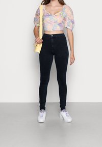 Puffihihat, pastellinvärinen kukkakuosis cropped-toppia, jossa on V-henkari; korkeavyötäröiset, tummansiniset skinny-farkut; yhdistettynä valkoisiin tennareihin ja keltaiseen laukkuun.