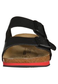 Black sandals featuring two adjustable straps, cork footbed, and a red accent on the sole. Textured material with a flat design.