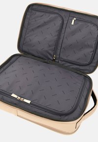 Borsa da viaggio beige con dettagli dorati, interno completamente foderato con motivo a logo ripetuto del marchio, due scomparti con zip e una maniglia robusta.