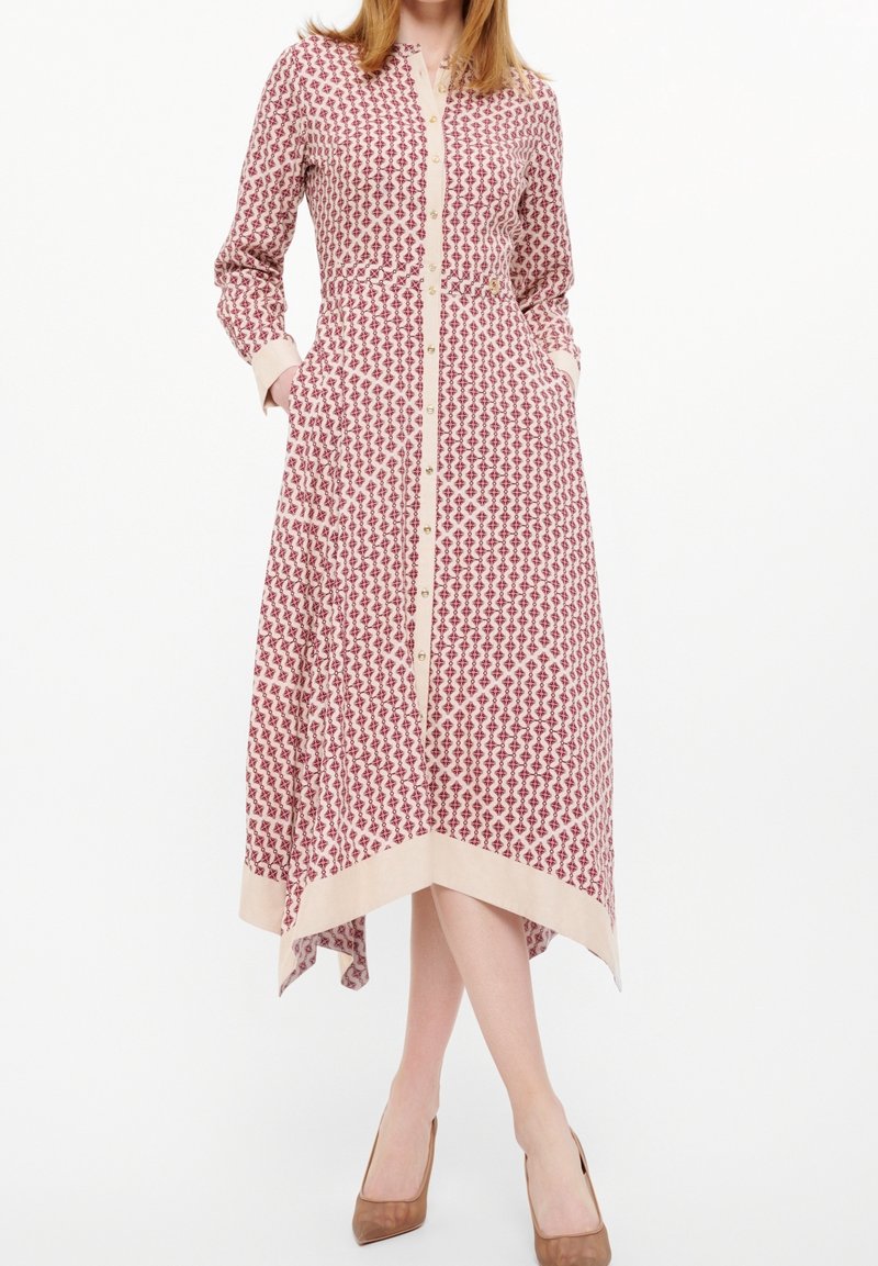 Robe à manches longues avec un motif géométrique rouge et crème, boutonnage à l'avant, poches latérales, et poignets et ourlet contrastants.