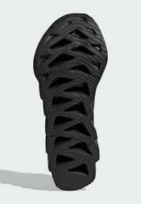 Black athletic shoe sole with zigzag grooves and cut-out patterns. Made of textured rubber, featuring a ridged surface for traction.