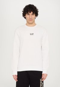 Hvid sweatshirt lavet af bomuld, med rund hals, lange ærmer og et lille sort EA7-logo på brystet. Glat tekstur.