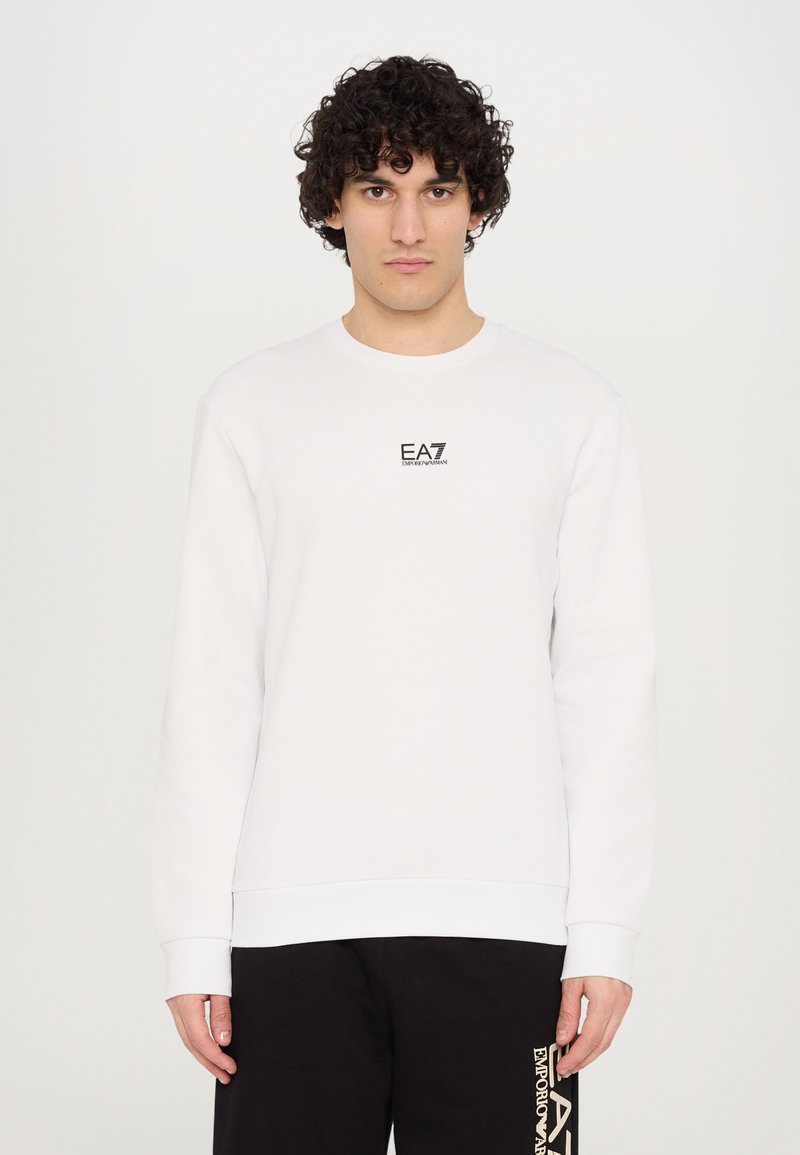 Hvid sweatshirt lavet af bomuld, med rund hals, lange ærmer og et lille sort EA7-logo på brystet. Glat tekstur.